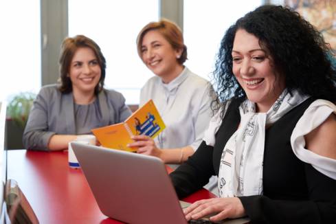 Служителки в централен офис на Лидл България в с. Равно Поле. На преден план е служителка с лаптоп, на заден плат две дами пия кафе.